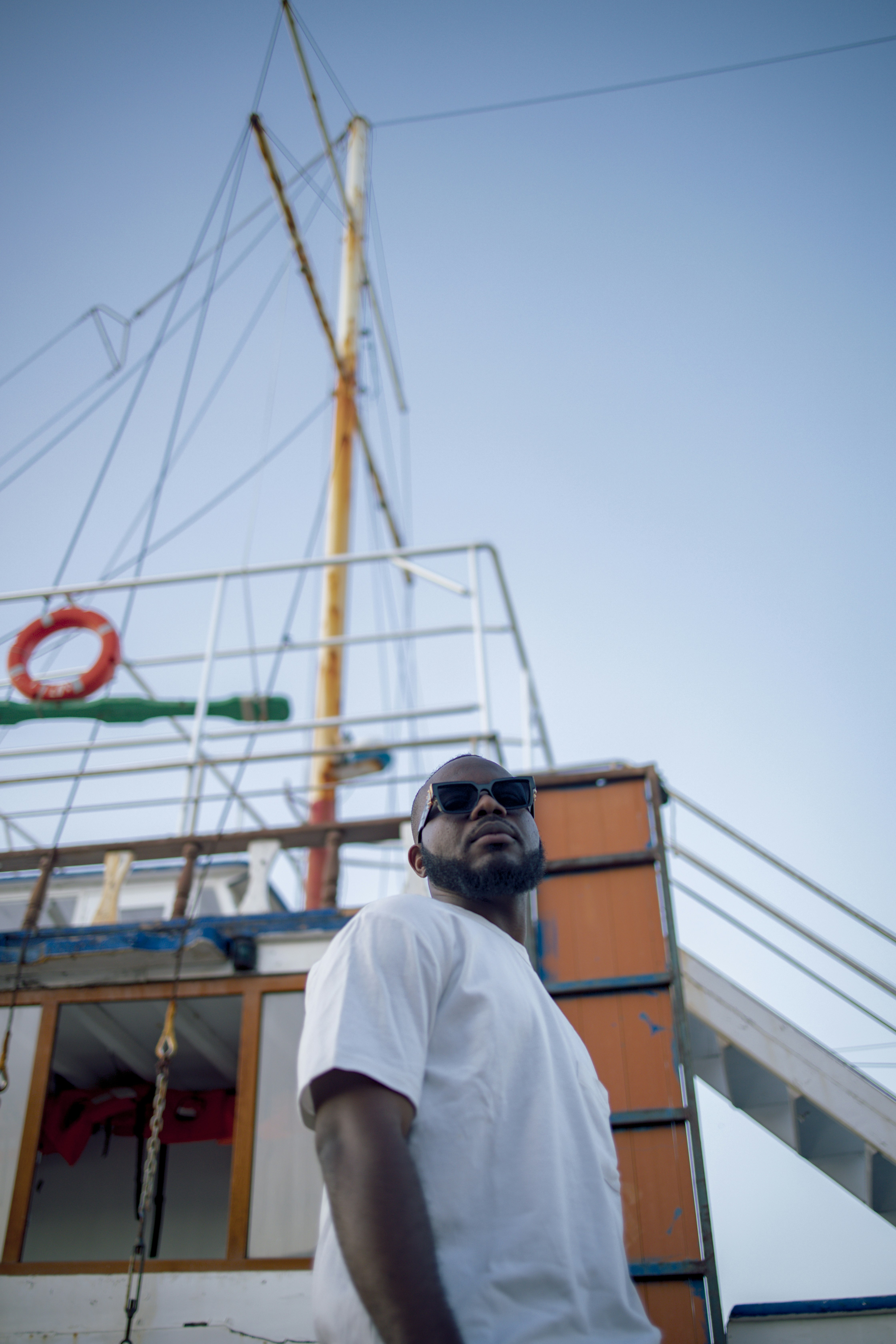 man in white shirt wearing black sunglasses standing near brown wooden boat during daytime